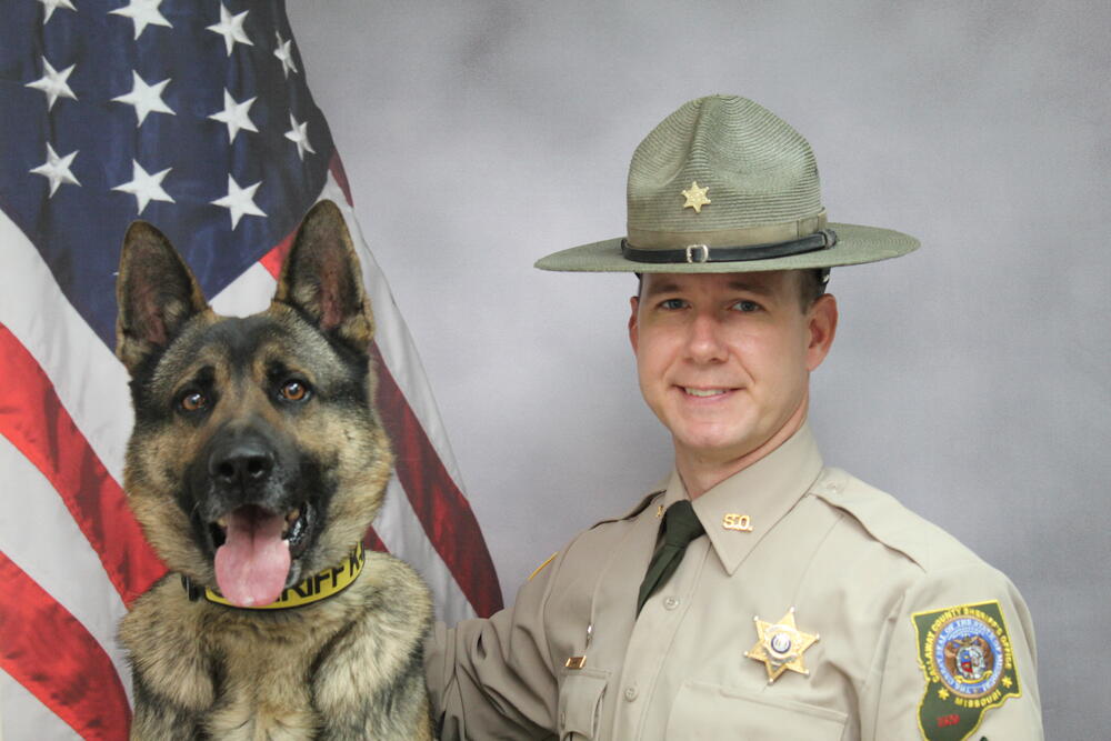 Sgt Corey Schmidt and K9 Krieger pictured in front of an American Flag.