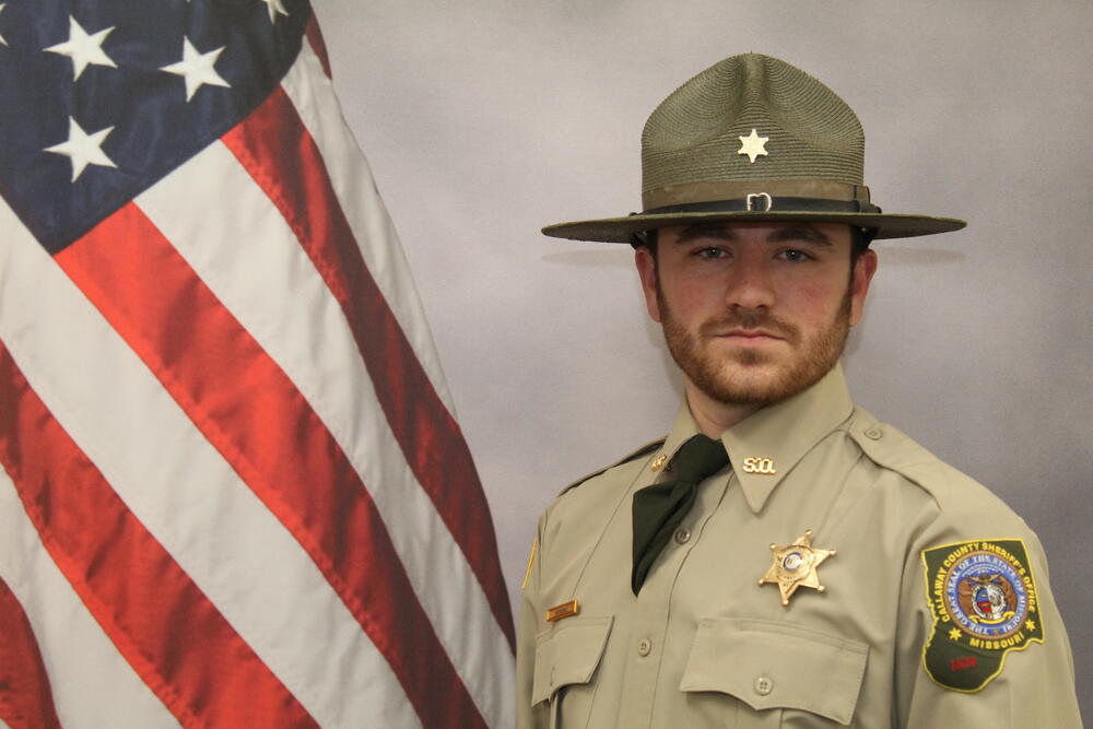 Photo of Deputy Jarred Kendall in uniform in front of an American Flag.