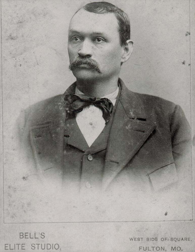 A black and white studio portrait of William H. Windsor wearing a three piece suit .  Writing on the image states that the photograph was taken at Bell's Elite Studio, west side of square, Fulton, MO.