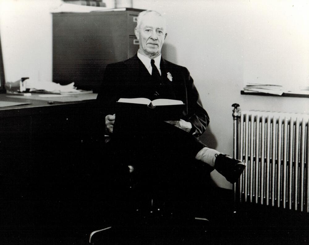 A black and white image of J. C. Owen.  Owen is seated in front of a desk and wearing a dark suit.