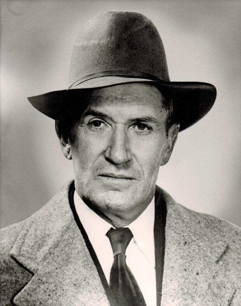 A black and white image of Paul Goodman.  Goodman is wearing a suit and tie with an overcoat and a Stetson hat.