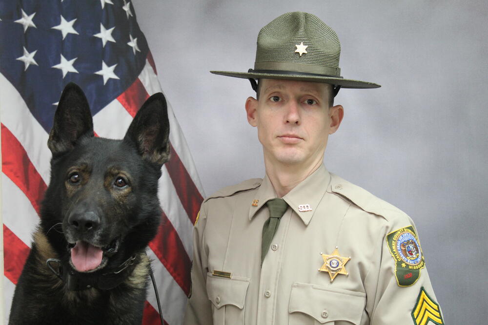 Sgt Alan LeBel and K9 Iro pictured in front of an American Flag.