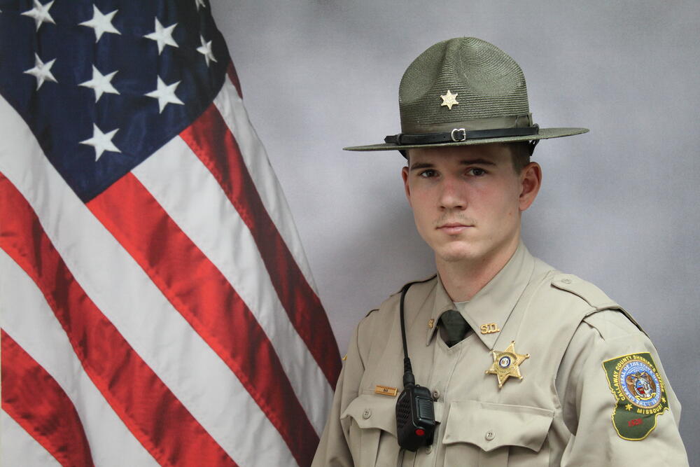Deputy Justin Bax pictured in front of an American Flag.