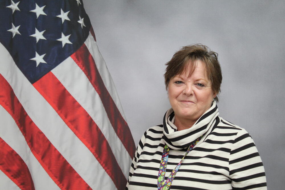 Administrative Assistant Brenda Ollar pictured in front of an American Flag..