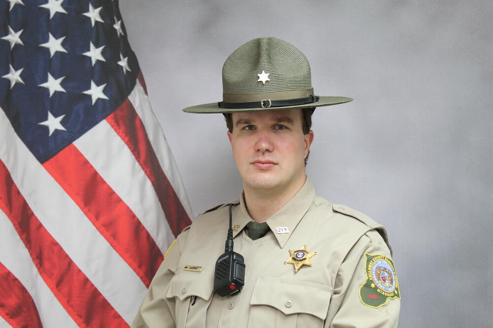Investigator Robbie Railton in uniform pictured in front of an American Flag.