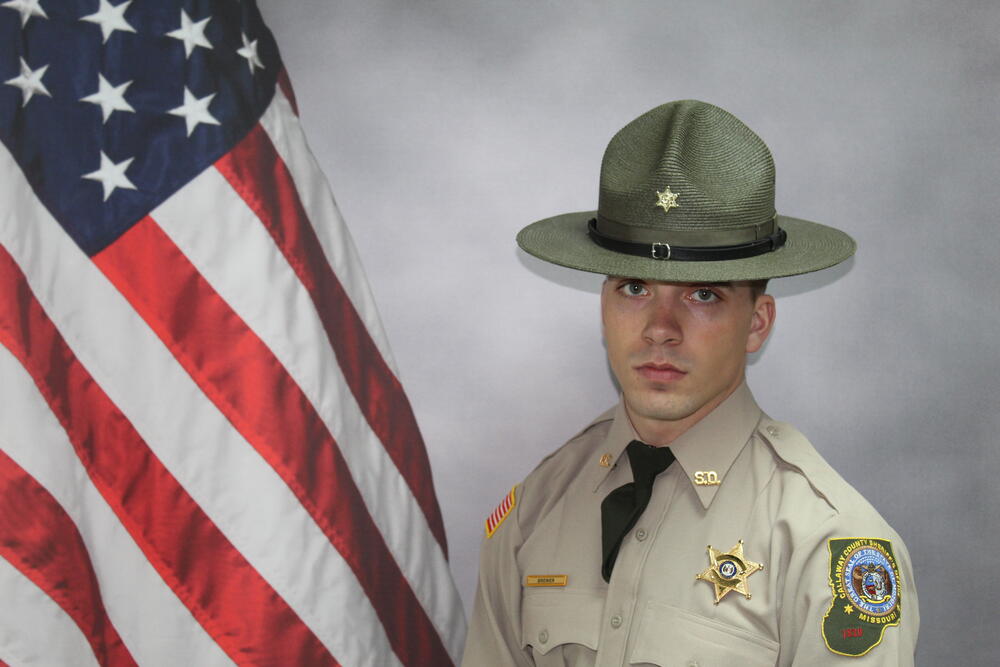 Deputy Logan Brewer pictured in uniform in front of an American Flag.