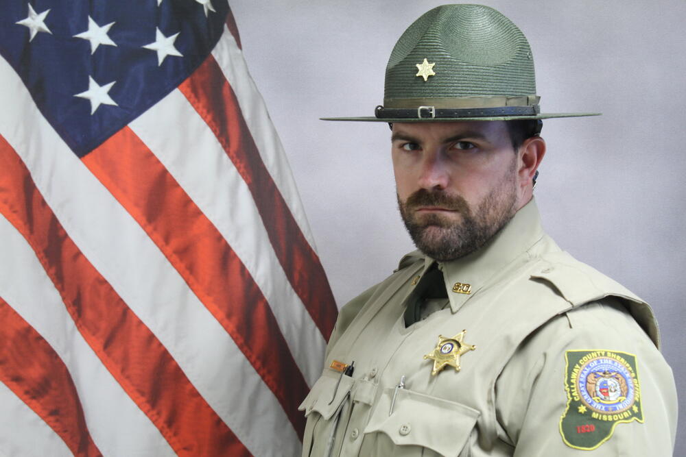 Deputy Pat Harris in uniform pictured in front of an American Flag.